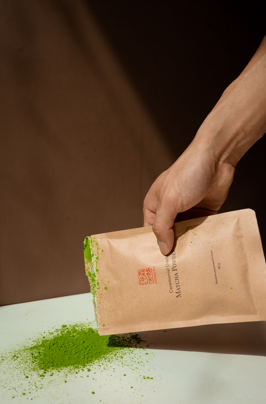 Product Picture A_Male_hand_holding_the_Shinrin_Tea_Matcha_Packaging_with_Matcha_on_the_surface